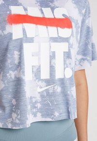 Camiseta corta de tie-dye azul con texto en blanco en negrita y un efecto de pintura en spray roja, con el logo de Nike en el dobladillo.