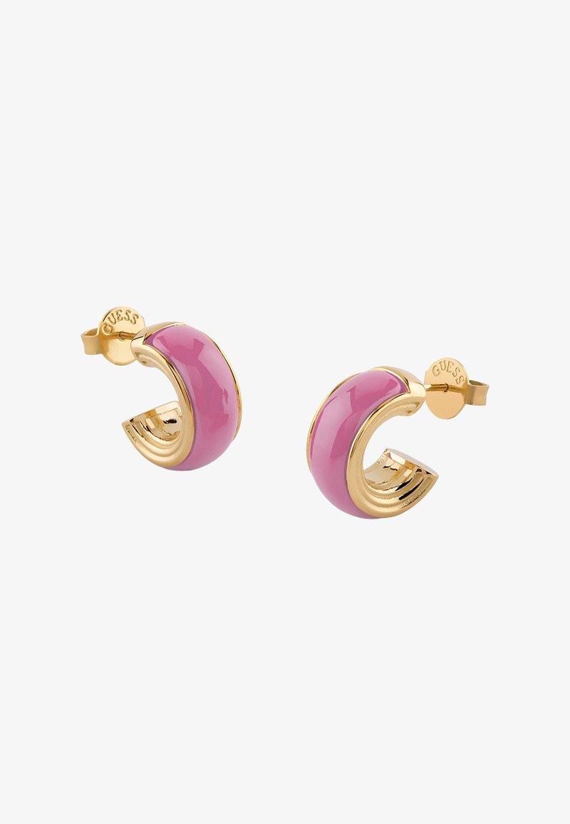 Σκουλαρίκια κρίκοι σε χρυσό τόνο με καμπυλωτές ροζ σμάλτο ενθέσεις και την λέξη "GUESS" χαραγμένη στις πλάτες τους, εμφανιζόμενα σε λευκό φόντο.