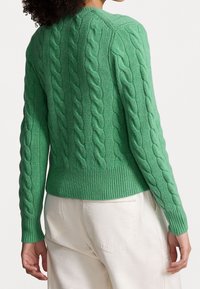 Grön kabelstickad tröja med texturerade mönster, ribbad manschetter och nederkant. Har en rund halsringning och en figurnära silhuett.
