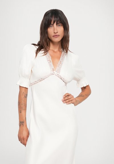 Witte jurk met korte pofmouwen, voorzien van een V-vormige halslijn en delicate kantafwerking rond de buste, wat een vloeiende silhouet creëert.