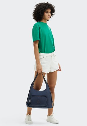 Dark blue hobo bag with a front zip pocket, glossy texture, soft fabric, and a shoulder strap. Keychain accent attached.