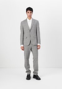 Completo da uomo grigio a scacchi con due bottoni, pantaloni coordinati, camicia bianca e scarpe in pelle nera. Tessuto morbido e vestibilità su misura.