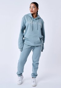 Felpa leggera blu con cappuccio e tasca frontale, decorata con un logo in bianco, abbinata a pantaloni da tuta coordinati con polsini elastici e vestibilità comoda.