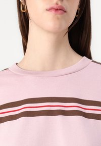 Sweatshirt di cotone light pink con scollatura tonda, caratterizzato da strisce orizzontali marroni e rosse sul petto. Tessuto morbido, vestibilità comoda.