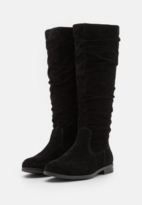 Par de botas altas de ante negro con tacones bajos y caños holgados, diseñadas para mujeres, mostradas sobre fondo blanco.