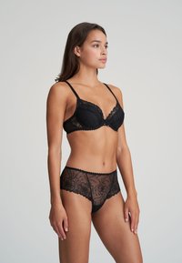 Czarny koronkowy stanik i pasujące przezroczyste majtki z haftem kwiatowym, falbaniastymi brzegami, regulowanymi ramiączkami i dopasowanym krojem.