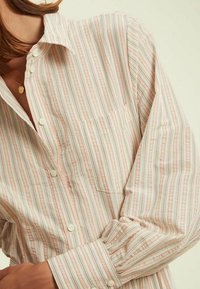 Chemise à boutons avec un motif rayé pastel léger en rose, bleu et blanc. Tissu en coton doux avec une poche sur la poitrine et des manches à poignets.