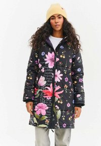 Černý květinový prošívaný kabát s v�ýraznými růžovými, fialovými a žlutými květy. Má zapínání na zip vpředu, dlouhé rukávy a elastické manžety.