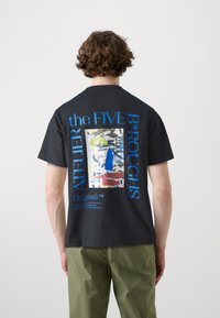 Μαύρο βαμβακερό t-shirt με μεγάλη γραφιστική σχεδίαση στην πλάτη με μπλε και πράσινες λεπτομέρειες και κείμενο, κοντά μανίκια και στρογγυλή λαιμόκοψη.