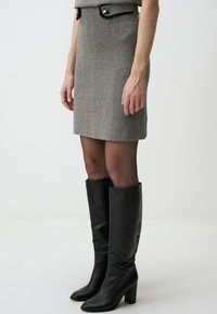 Mini gonna a motivo houndstooth grigio con una silhouette aderente, abbinata a stivali neri in pelle con tacco alto. La gonna presenta una cintura con dettaglio a bottone.