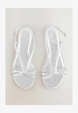 Hopeasävyiset metalliset sandaalit, joissa on hihnallinen muotoilu. Sandaaleissa on kaksi riviä kirkaita strassikiviä varpaiden kohdalla ja säädettävä nilkkahihna.