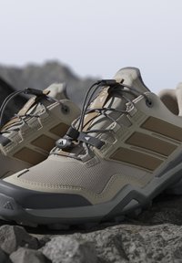 Scarpe da trekking durevoli beige e marroni con sistema di allacciatura rapida appoggiate su terreno roccioso, progettate per attività all'aperto su sentieri.