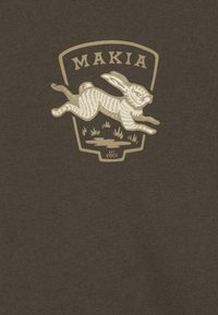 Hnedé bavlnené tričko s krémovou grafikou skáčuceho zajaca, nad ktorým je nápis "MAKIA" a pod ním "EST 2001".