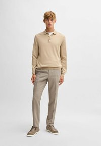Polo in maglia beige con una patta a tre bottoni, abbinato a dei pantaloni grigi chiari a quadri e scarpe beige con suola bianca.