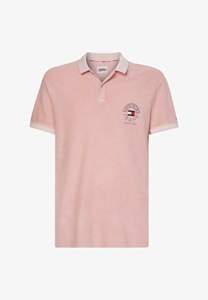 Polo rose clair à manches courtes avec col blanc et bordure aux manches, avec logo Tommy Jeans et emblème du drapeau sur la poitrine.