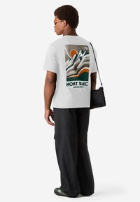 Camiseta de algodón blanca con un diseño gráfico de montañas y un sol en verde, naranja y beige, con el texto "MONT BLANC" en la parte posterior.