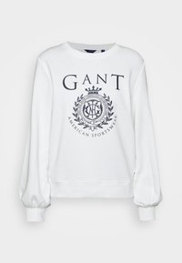 Sweatshirt blanc à manches bouffantes, avec un logo imprimé et un design de blason bleu marine. Fabriqué en tissu mélangé de coton.