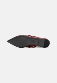 Roter spitzer Schuh aus glattem synthetischem Material, mit drei verstellbaren Riemen und einer strukturierten schwarzen Gummisohle. Minimalistische Markenkennzeichnung.