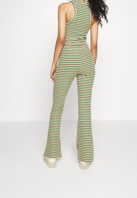 Gestreept twee-delig set bestaande uit een aansluitende tanktop en uitlopende broek. Kleuren zijn groen, rood en geel. Geribbelde textuur.