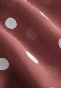 Austas audinys turtingos bordo spalvos, dekoruotas dideliais baltais taškais. Paviršius yra lygus ir šiek tiek permatomas, su matomais raukšlėmis.