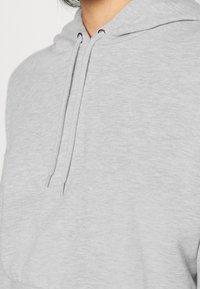 Šedá mikina s kapucí na šňůrku, vyrobená z měkké, strukturované tkaniny a s kovovými očky na šňůrky.