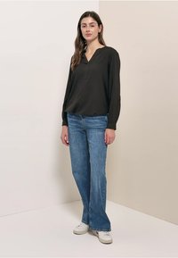 Blouse noire à manches longues avec un col en V et une coupe décontractée, associée à un jean à jambes larges bleu clair et des baskets blanches. Texture de tissu lisse.