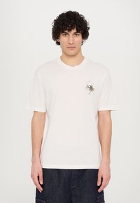 Camiseta de algodón blanca con mangas cortas, escote redondo y un pequeño detalle bordado de una palmera y un logo en el lado izquierdo del pecho.