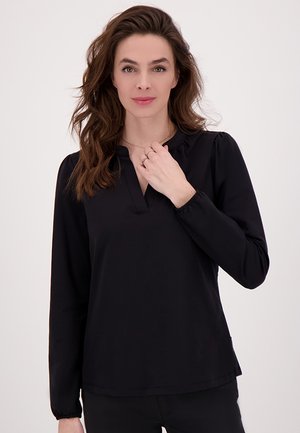 Zwarte blouse met lange mouwen, een V-hals en geplooide manchet, met een soepele textuur en een ontspannen pasvorm, weergegeven tegen een lichte achtergrond.