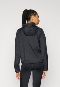 Μαύρο ελαφρύ μπουφάν με κουκούλα, με υφή, ελαστικές μανσέτες και κοντό σχέδιο, φορεμένο με μαύρες κολάν.