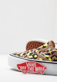 Sneaker slip-on Vans con stampa leopardata marrone e neon, dotata di suola bianca, accenti laterali elasticizzati e un'etichetta rossa "Off The Wall".