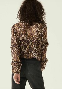 Kwiatowa bluzka na ciemnym tle, z falbaniastym dołem i rękawami, wykonana z lekkiego, przezroczystego materiału. Połączona z czarnymi dżinsami.