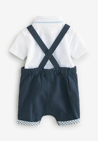 Bílé polo s modrými detaily v kombinaci s tmavě modrými šortkami s nastavitelnými kšandami a vzorovaným lemem. Materiál s texturou po celém obvodu.