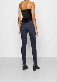 Svart strapless topp med rynkning och blommönster, kombinerad med mörka jeans i skinny-modell och svarta klackstövlar, sedd bakifrån.