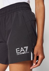 Svarte sports shorts med elastisk midjebånd, med hvit EA7 Emporio Armani-logo og sidelommer for funksjonalitet.