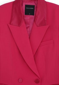 Blazer fuchsia avec un col en satin, devant double boutonnage, design structuré, poches latérales et texture de tissu lisse. Étiquette de marque visible.