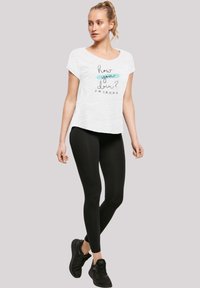 Hvit kortermet t-skjorte med trykt design "how you doin'?" i blått og svart, sammen med svarte leggings og svarte treningssko.