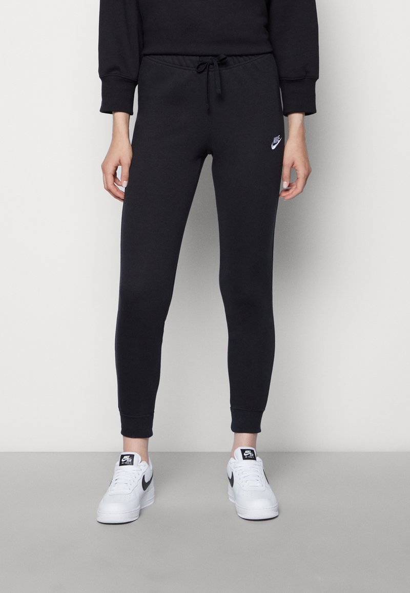 Svarta tapered joggers med elastisk midja och dragsko, med en liten vit Nike-logotyp på vänster lår. Matchat med vita sneakers.