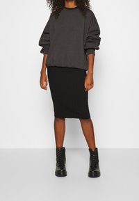 Ciemnoszara, oversize bluza z długimi rękawami, w zestawie z czarną prążkowaną spódnicą ołówkową i czarnymi, sznurowanymi butami wojskowymi.