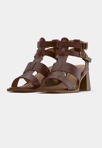Καφέ δερμάτινα σανδάλια με τακούνι και ανοιχτή μύτη, με πολλαπλά σχέδια λουριών και ρυθμιζόμενες αγκράφες. Στερεό τακούνι με υφή αυλακώσεων.