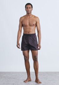 Short de bain noir avec une taille élastique et un cordon de serrage. Le matériau semble léger, et le design est simple, sans motifs ni accents.