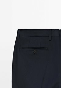 Navy pinstriped trousers feature a flat front, belt loops, and a single back pocket with a button closure. Smooth fabric texture.