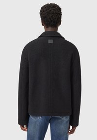 Zwarte wol jacket met een kraag, verlaagde schouders en een vierkant label aan de achterkant. Draag het over een blauwe spijkerbroek en laat een strakke, minimalistische uitstraling zien.