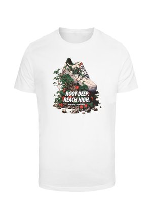 Biely tričko s grafikou tenisky obklopenej zeleňou a kvetmi, s nápisom "KOREŇ HLBOKO. DOSAHUJ VYSOKO." výrazne zobrazeným.
