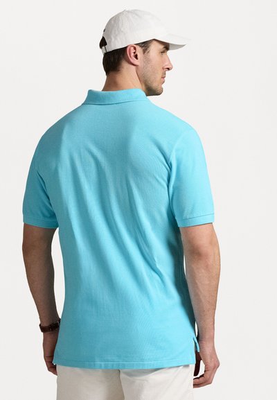 Ανοιχτό μπλε πουκάμισο πόλο με κοντά μανίκια, κολάρο και πλαϊνές σχισμές. Φορεμένο με λευκό καπέλο, διαθέτει υφασμάτινη υφή.