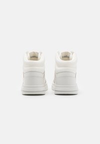 Sneakers alta in pelle bianca e tela. Collo imbottito, lati testurizzati e suola in gomma. Presentano un design minimalista senza loghi visibili.