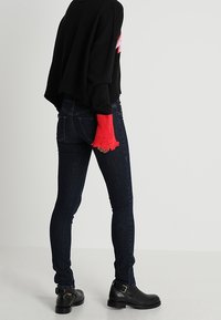 Jersey negro de gran tamaño con puños rojos de flecos, combinado con jeans ajustados azul oscuro y botas negras de tobillo con detalle de hebilla.