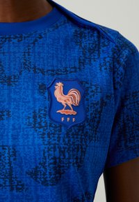 Blue sports shirt featuring a textured pattern, round neck, and a crest depicting a rooster with the initials "FFF" in white.