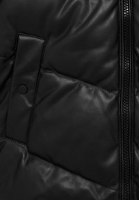 Primer plano de una chaqueta de cuero negra acolchada con detalles de cremallera y bolsillo con botón a presión.