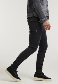 Slim-fit svarta jeans med en jämn yta, subtila detaljer på framfickorna, tillsammans med svarta mockasneakers med en krämfärgad sula.