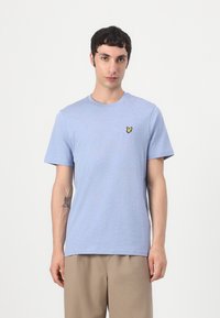 T-shirt bleu clair à manches courtes en coton doux avec un col rond et un petit logo jaune brodé sur la poitrine gauche.